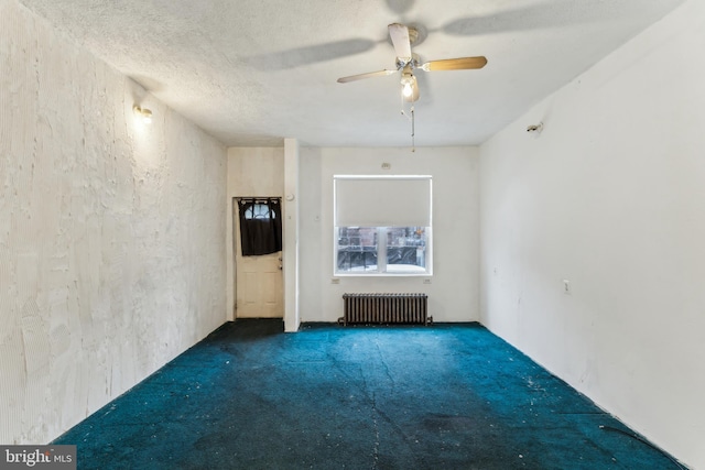 spare room with ceiling fan, dark carpet, radiator heating unit, and a textured ceiling