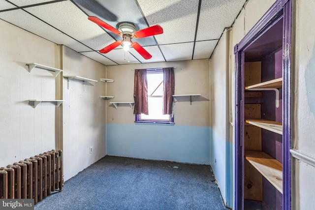 empty room featuring carpet flooring, ceiling fan, a drop ceiling, and radiator heating unit