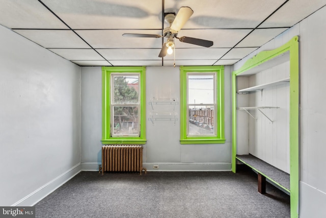 interior space with a drop ceiling, carpet floors, ceiling fan, radiator heating unit, and a closet