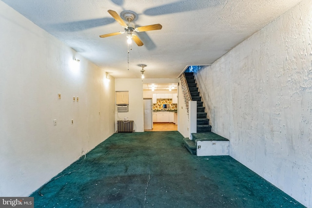 unfurnished living room with radiator heating unit, a textured ceiling, dark carpet, and ceiling fan