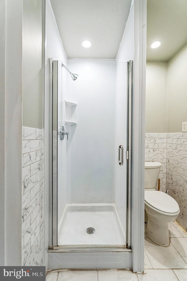 bathroom featuring a shower with door, toilet, and tile walls