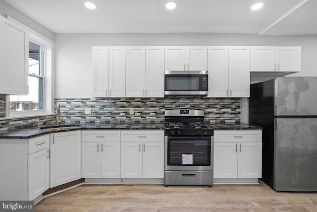 kitchen featuring appliances with stainless steel finishes, backsplash, sink, dark stone countertops, and white cabinetry