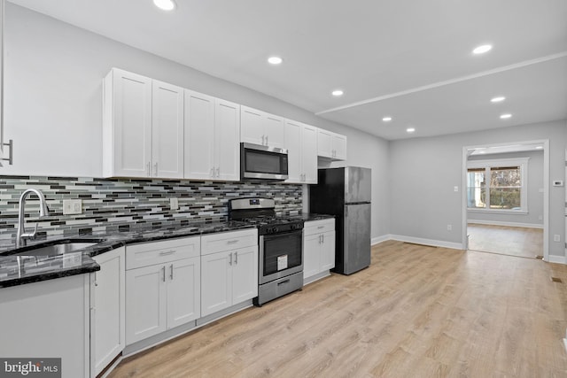 kitchen featuring white cabinets, stainless steel appliances, dark stone counters, and sink