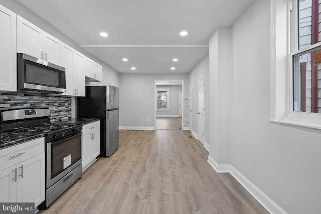 kitchen featuring decorative backsplash, white cabinets, light wood-type flooring, and appliances with stainless steel finishes