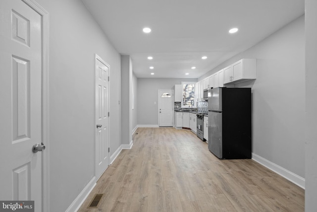 kitchen with white cabinets, light hardwood / wood-style floors, stainless steel appliances, and tasteful backsplash