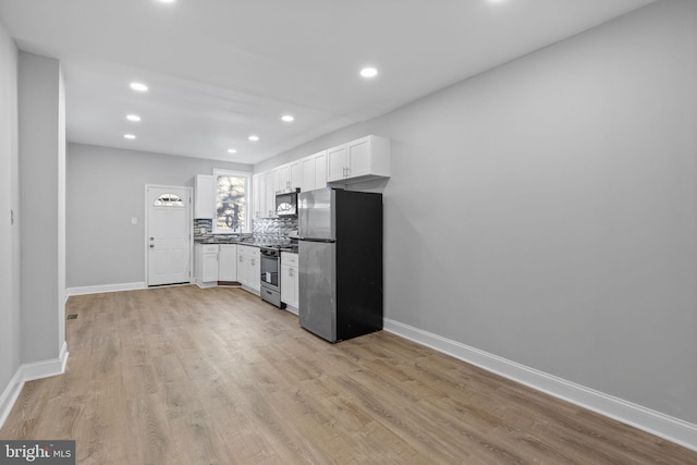 kitchen featuring backsplash, white cabinetry, stainless steel appliances, and light hardwood / wood-style floors