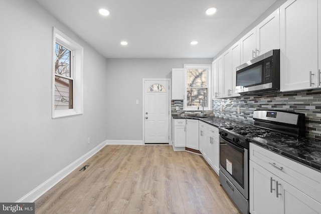 kitchen with white cabinetry, sink, light hardwood / wood-style flooring, backsplash, and appliances with stainless steel finishes