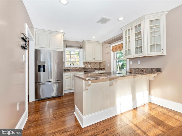 kitchen with kitchen peninsula, stainless steel fridge, sink, white cabinetry, and a breakfast bar area