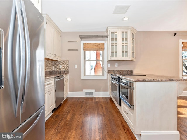 kitchen featuring dark hardwood / wood-style flooring, tasteful backsplash, dark stone counters, stainless steel appliances, and white cabinets