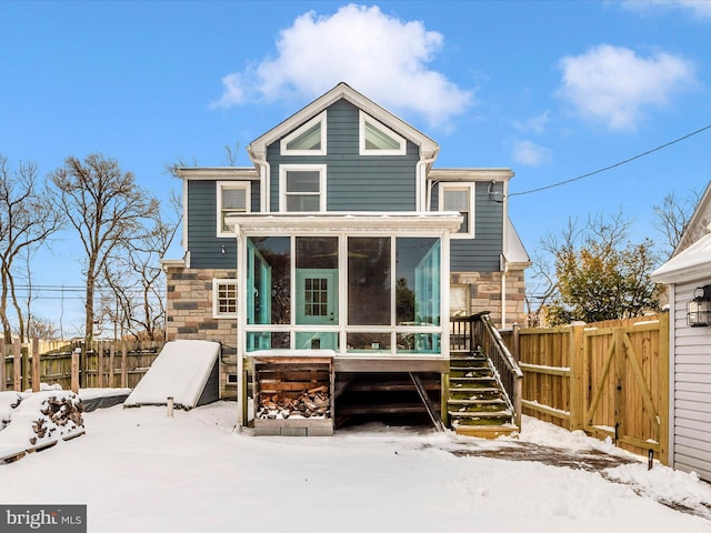 snow covered back of property featuring a sunroom