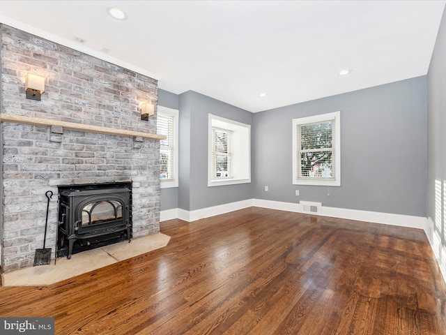 unfurnished living room with hardwood / wood-style flooring, a wood stove, and a wealth of natural light