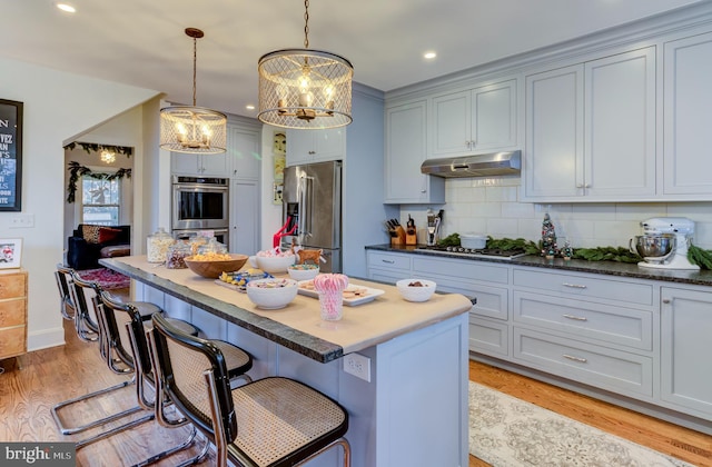 kitchen featuring a center island, a kitchen breakfast bar, hanging light fixtures, decorative backsplash, and appliances with stainless steel finishes