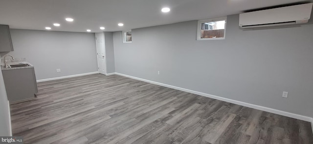 basement with light hardwood / wood-style floors, an AC wall unit, and sink