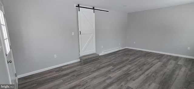 empty room with a barn door, dark hardwood / wood-style flooring, and a baseboard heating unit