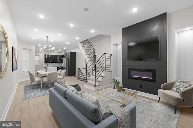 living room with light wood-type flooring, a large fireplace, and an inviting chandelier