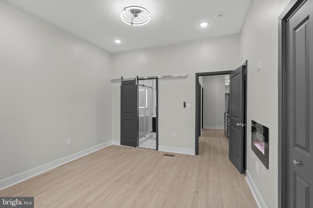 unfurnished bedroom featuring light wood-type flooring and a barn door