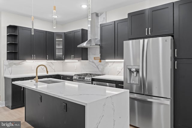 kitchen with light stone countertops, sink, wall chimney exhaust hood, a kitchen island with sink, and appliances with stainless steel finishes