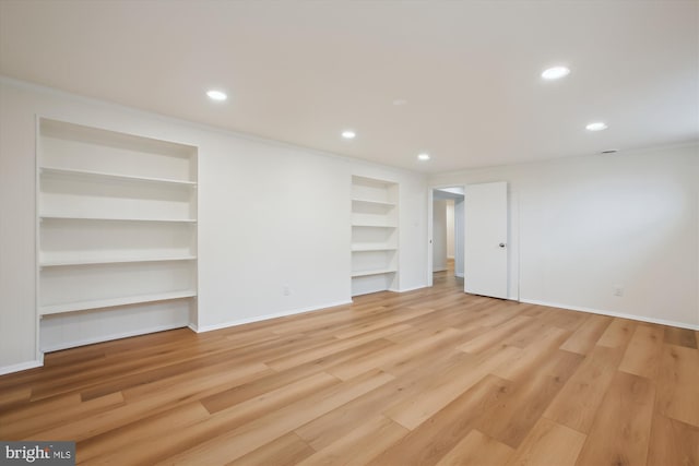 empty room featuring built in shelves, ornamental molding, and light wood-type flooring