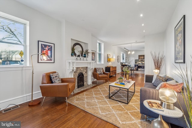 living room with a chandelier, wood-type flooring, and a brick fireplace