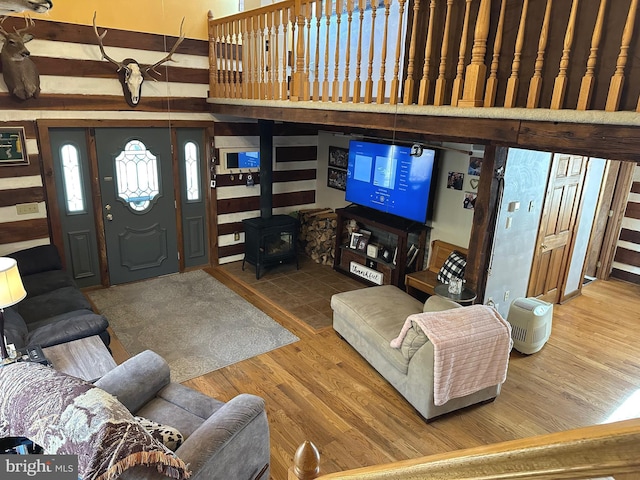 living room featuring wood-type flooring, a wood stove, and a towering ceiling