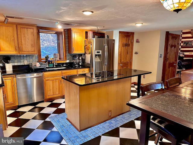 kitchen featuring sink, stainless steel appliances, backsplash, track lighting, and a kitchen island