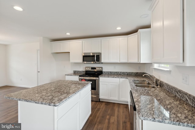 kitchen with appliances with stainless steel finishes, sink, white cabinets, dark hardwood / wood-style floors, and a kitchen island