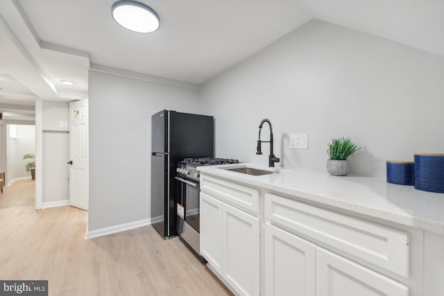 kitchen featuring stainless steel gas range oven, white cabinets, sink, light hardwood / wood-style flooring, and light stone countertops