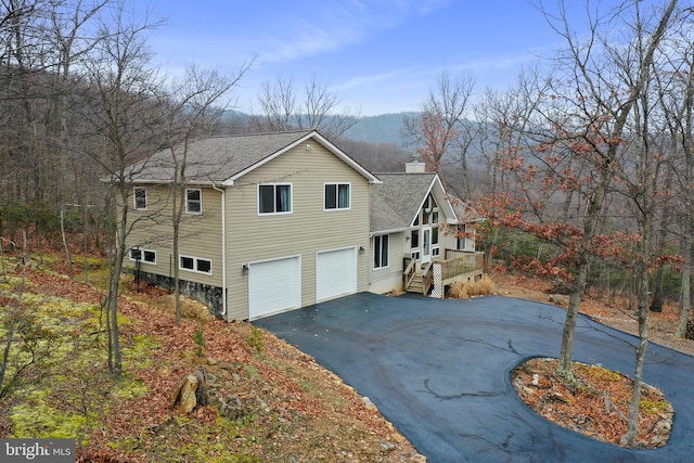 view of side of property with driveway, a garage, a chimney, and roof with shingles