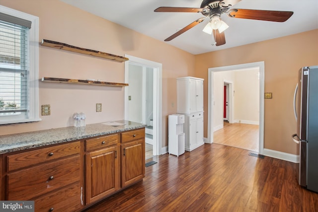 kitchen featuring stainless steel refrigerator, light stone counters, dark hardwood / wood-style flooring, and ceiling fan