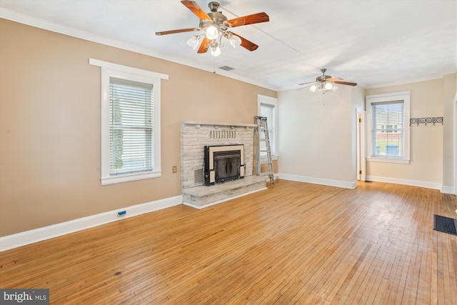 unfurnished living room featuring a wood stove, light hardwood / wood-style flooring, ceiling fan, and ornamental molding