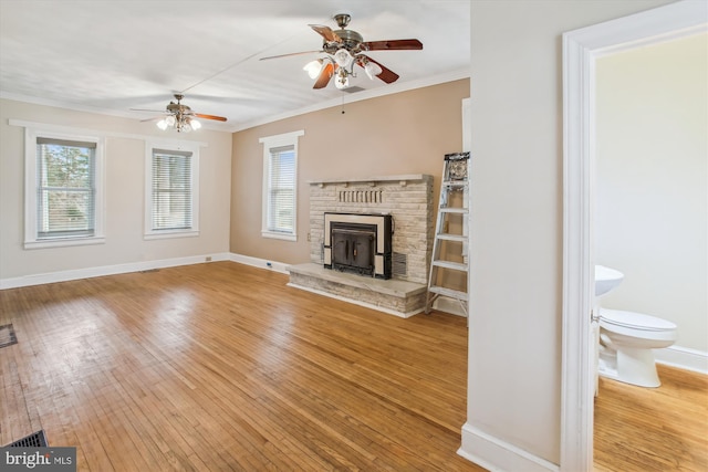 unfurnished living room featuring light hardwood / wood-style floors, a wood stove, plenty of natural light, and ceiling fan