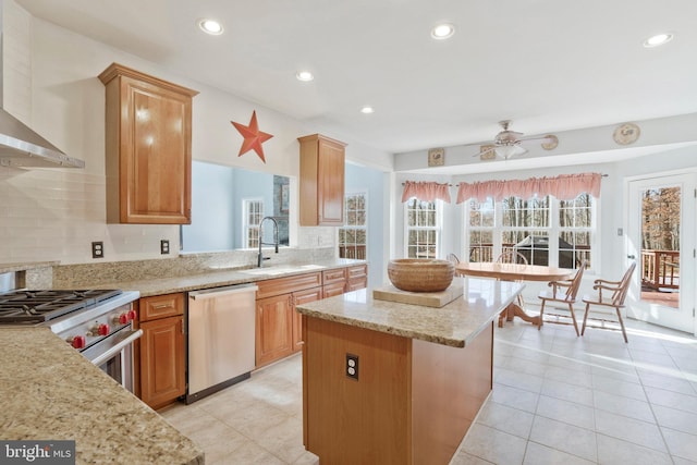 kitchen with appliances with stainless steel finishes, light stone counters, wall chimney exhaust hood, sink, and a center island