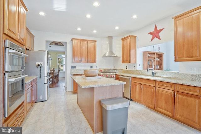 kitchen with appliances with stainless steel finishes, light stone counters, sink, wall chimney range hood, and a center island