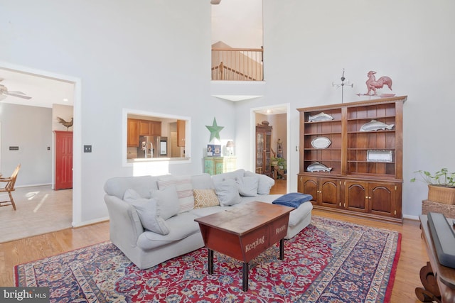 living room featuring a high ceiling, light wood-type flooring, and ceiling fan