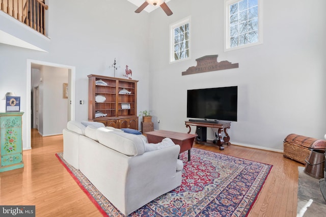 living room with ceiling fan, a high ceiling, and light wood-type flooring