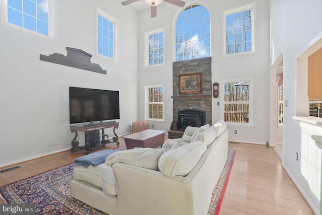 living room with ceiling fan, a fireplace, a high ceiling, and light hardwood / wood-style flooring