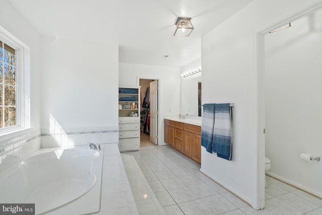 bathroom with tile patterned flooring, vanity, toilet, and tiled tub