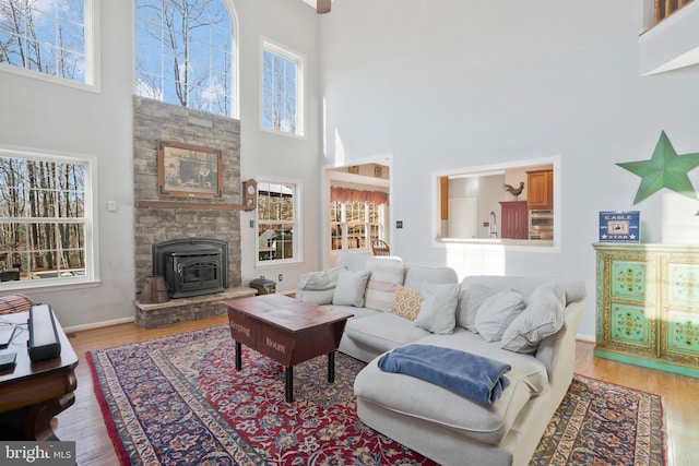 living room with light wood-type flooring, a towering ceiling, and a wood stove