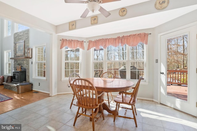 tiled dining room featuring a wood stove, ceiling fan, and a healthy amount of sunlight