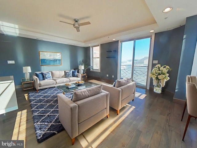 living room featuring dark hardwood / wood-style flooring, a tray ceiling, and ceiling fan