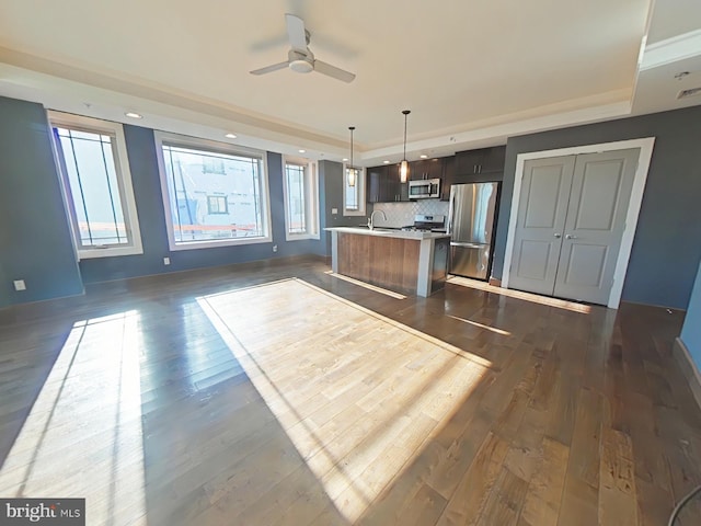 kitchen with hanging light fixtures, a kitchen island with sink, appliances with stainless steel finishes, and a tray ceiling