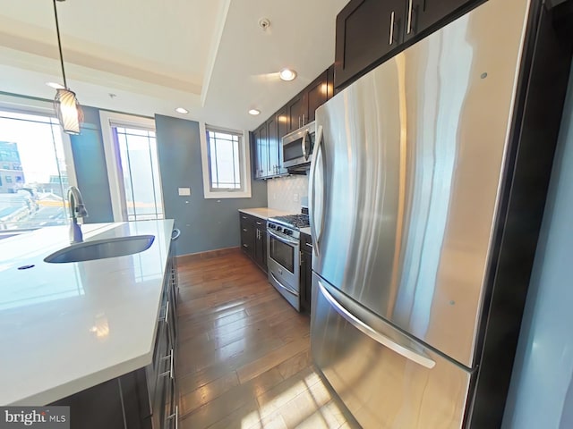 kitchen with sink, dark hardwood / wood-style floors, decorative backsplash, appliances with stainless steel finishes, and decorative light fixtures