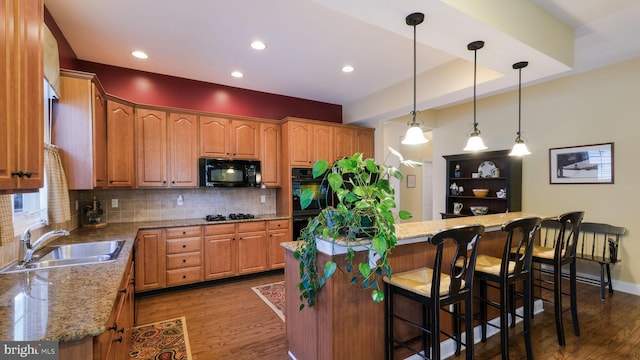 kitchen with light stone countertops, sink, decorative light fixtures, a breakfast bar, and black appliances