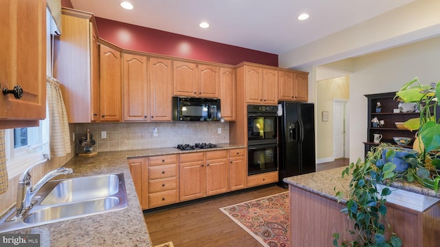 kitchen featuring decorative backsplash, light stone countertops, light wood-type flooring, sink, and black appliances