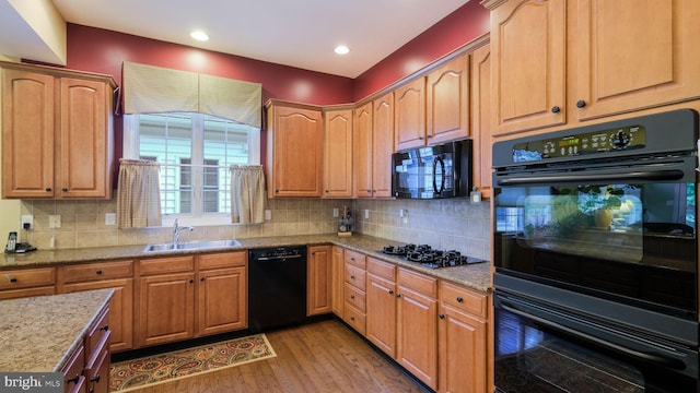 kitchen featuring tasteful backsplash, light stone counters, sink, black appliances, and light hardwood / wood-style floors