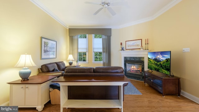 living room featuring a high end fireplace, light hardwood / wood-style flooring, ceiling fan, and crown molding