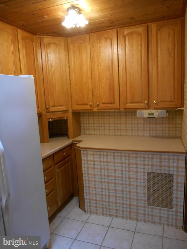 kitchen featuring light tile patterned floors, brown cabinets, freestanding refrigerator, light countertops, and backsplash