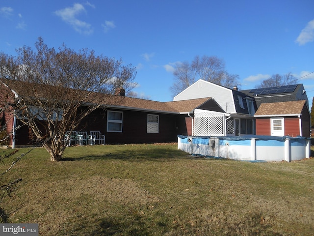 back of property with a yard, a chimney, roof mounted solar panels, and a covered pool