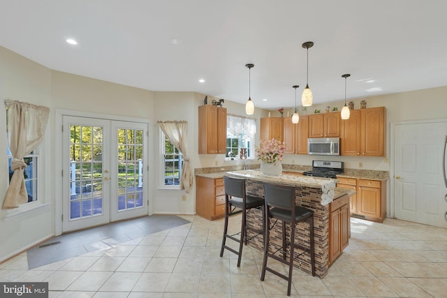 kitchen featuring appliances with stainless steel finishes, french doors, light stone counters, a center island, and light tile patterned flooring