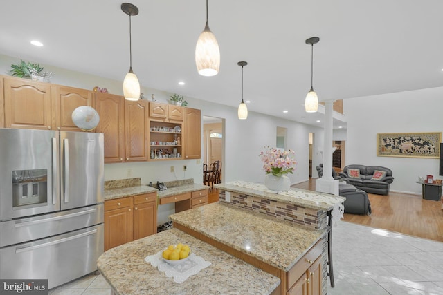 kitchen featuring pendant lighting, a center island, stainless steel fridge, light tile patterned flooring, and light stone counters